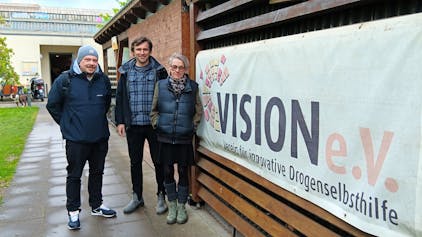 Drei Personen stehen vor einem Banner des Vision-Vereins.