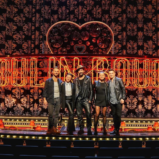 Fünf Personen stehen auf der Bühne vor einem Vorhang und dem Schriftzug "Moulin Rouge"
