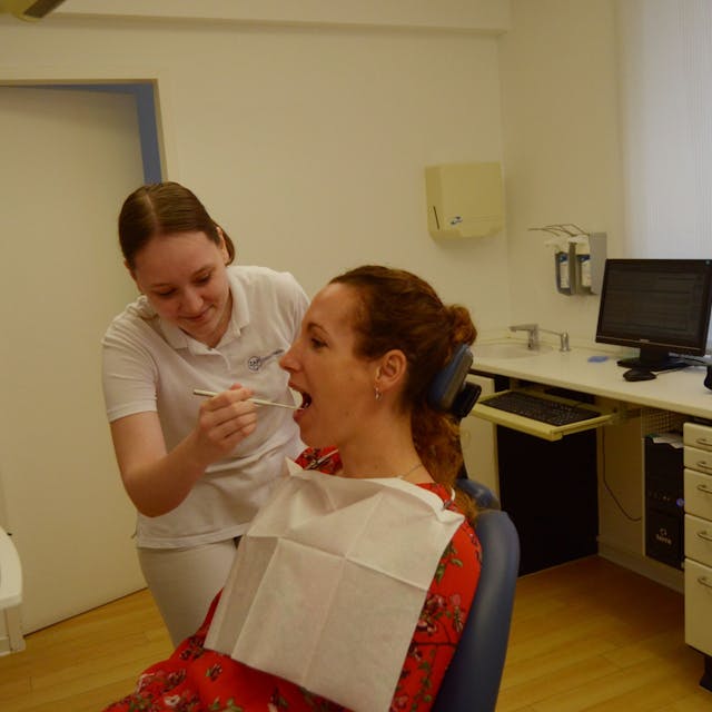 Celine Doerr blickt in der Zahnarztpraxis, in der sie arbeitet, in den Mund einer Patientin, die auf dem Behandlungsstuhl sitzt.