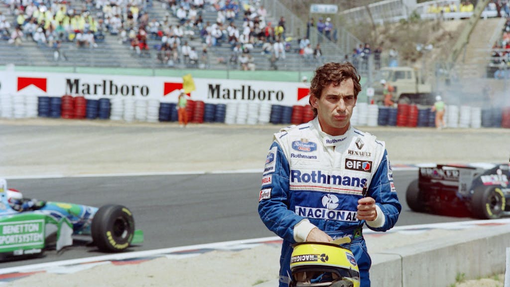 Ayrton Senna steht nach seinem Ausscheiden aus dem Pacific Grand Prix der Formel 1 der Rennstrecke, im Hintergrund fahren die anderen Autos.