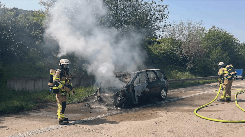 Zwei Feuerwehrleute löschen den brennenden Wagen auf der A4.