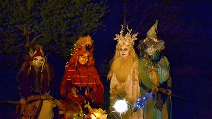 Vier farbenfroh kostümierte Hexen mit leuchtenden Fackeln in der Dunkelheit.