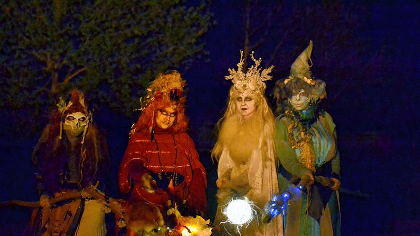 Vier farbenfroh kostümierte Hexen mit leuchtenden Fackeln in der Dunkelheit.