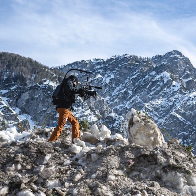 Eine Kamerafrau läuft über einen Haufen Schnee in den Bergen.