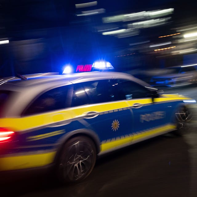 Ein Polizeifahrzeug fährt im Rahmen mit Blaulicht an einem Gebäude vorbei.