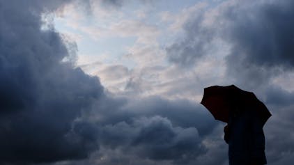 Ein Mann geht mit einem Regenschirm vor aufziehenden dunklen Wolken spazieren. (Symbolfoto)