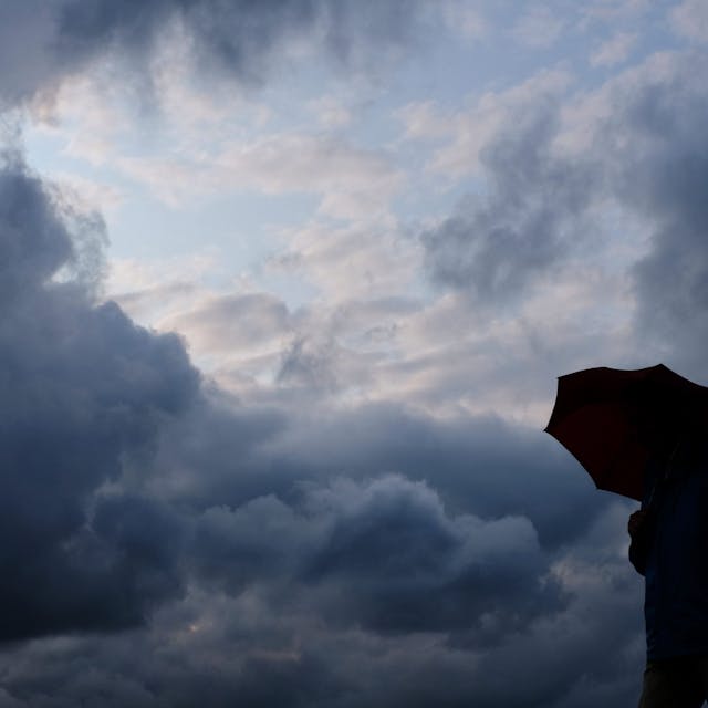 Ein Mann geht mit einem Regenschirm vor aufziehenden dunklen Wolken spazieren. (Symbolfoto)