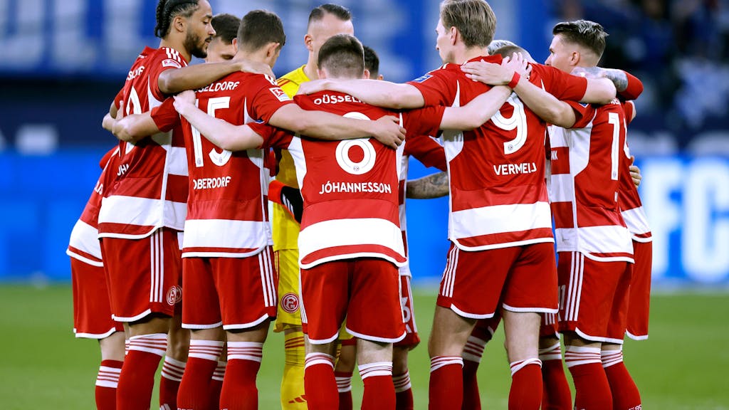 Das Team von Fortuna Düsseldorf steht vor dem Anpfiff des Auswärtsspiels beim FC Schalke 04 Arm in Arm am Mittelkreis zusammen.