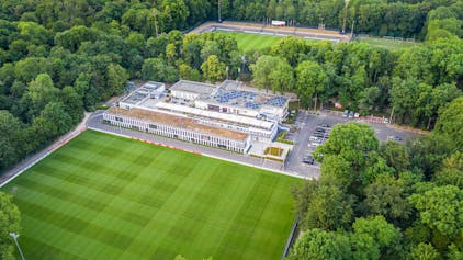 Das Geißbockheim genannte Clubhaus des Fußballvereins 1. FC Köln im Äußeren Grüngürtel mit einem Rasen-Trainingsplatz im Vordergrund und dem Franz-Kremer-Stadion im Hintergrund. Zu sehen auf einer Luftaufnahme, die mithilfe einer Drohne hergestellt wurde.