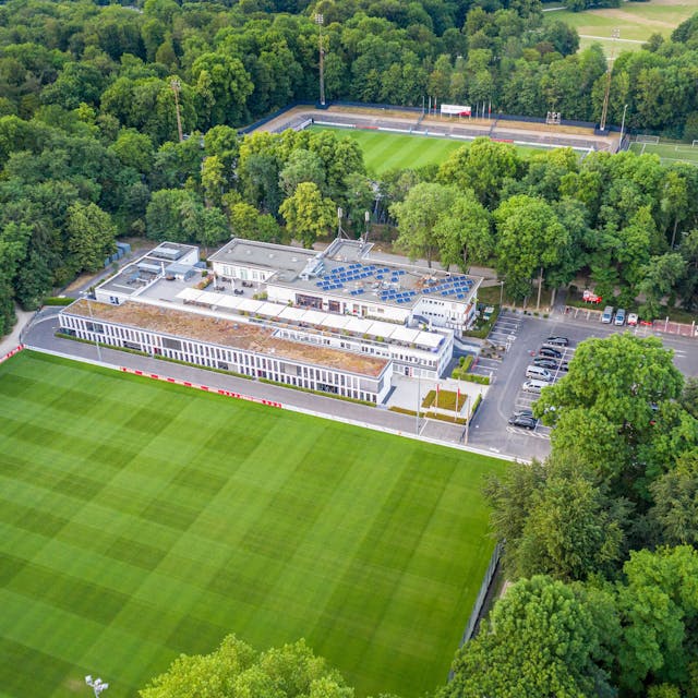 Das Geißbockheim genannte Clubhaus des Fußballvereins 1. FC Köln im Äußeren Grüngürtel mit einem Rasen-Trainingsplatz im Vordergrund und dem Franz-Kremer-Stadion im Hintergrund. Zu sehen auf einer Luftaufnahme, die mithilfe einer Drohne hergestellt wurde.