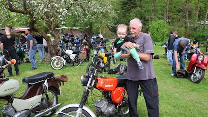 Ein älterer Herr zeigt einem kleinen Kind ein Motorrad.