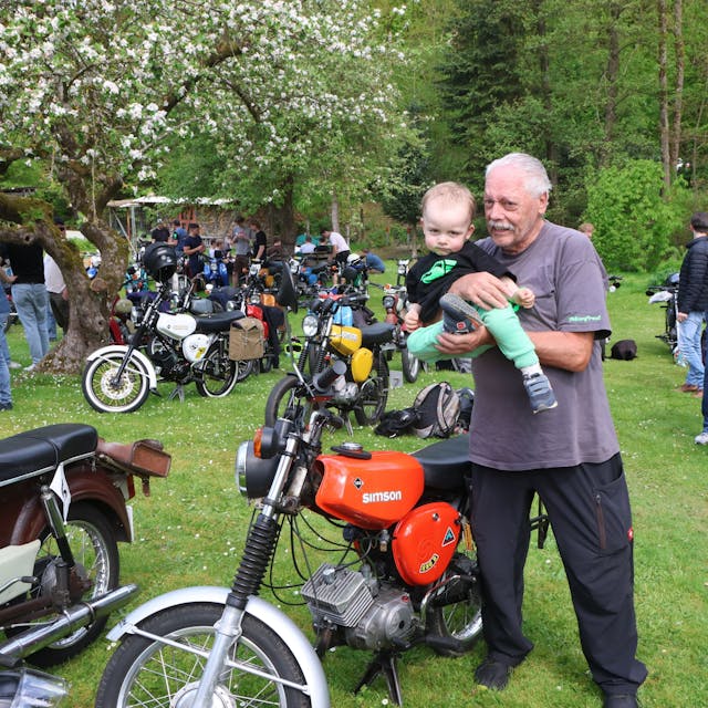Ein älterer Herr zeigt einem kleinen Kind ein Motorrad.