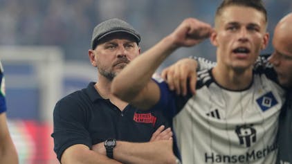 Steffen Baumgart verfolgt mit verschränkten Armen, wie seine Spieler sich nach dem Derbysieg von den Fans feiern lassen.