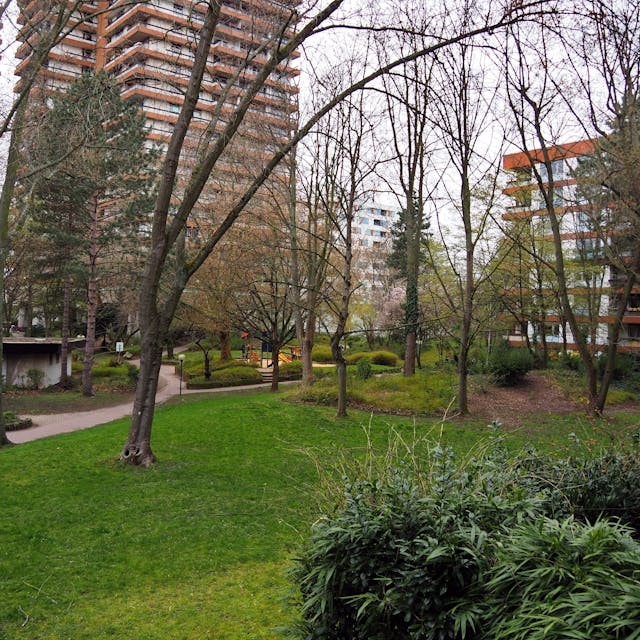 Blick auf den grünen Park mit hohen Bäumen, umgeben von den Wohnhochhäusern des Wohnpark Bayenthals. Foto von Stephanie Broch.