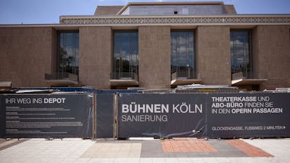 Plakate mit der Aufschrift „Bühnen Köln Sanierung“ hängen am Zaun rund um Oper und Schauspielhaus. Knapp sieben Jahre ist diese Aufnahme bereits alt, abgeschlossen ist die Sanierung immer noch nicht. (Archivbild)