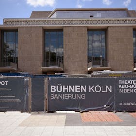 Plakate mit der Aufschrift „Bühnen Köln Sanierung“ hängen am Zaun rund um Oper und Schauspielhaus. Knapp sieben Jahre ist diese Aufnahme bereits alt, abgeschlossen ist die Sanierung immer noch nicht. (Archivbild)