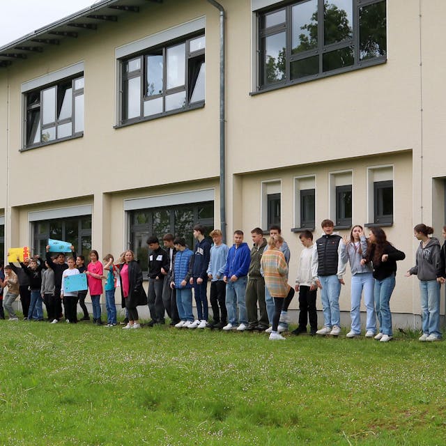 Schülerinnen und Schüler, Lehrkräfte sowie Niederkasseler Bürgerinnen und Bürger haben mit einer Menschenkette um die Alfred-Delp-Realschule Demokratie, Menschenrechte und Vielfalt demonstriert.