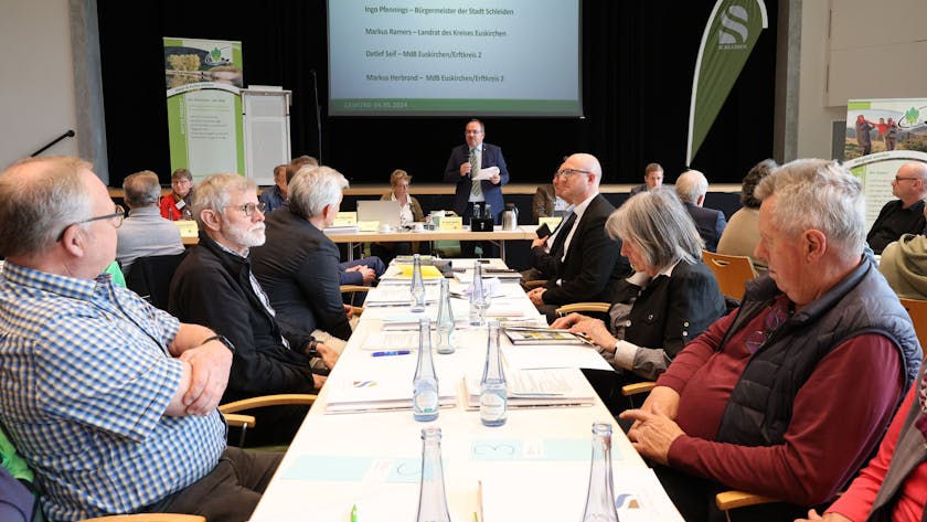 Zahlreiche Personen sitzen bei der Tagung des Eifelvereins im Kursaal Gemünd an Tischen. In der Mitte steht Hauptvorsitzender Dr. Ralf Nolten.