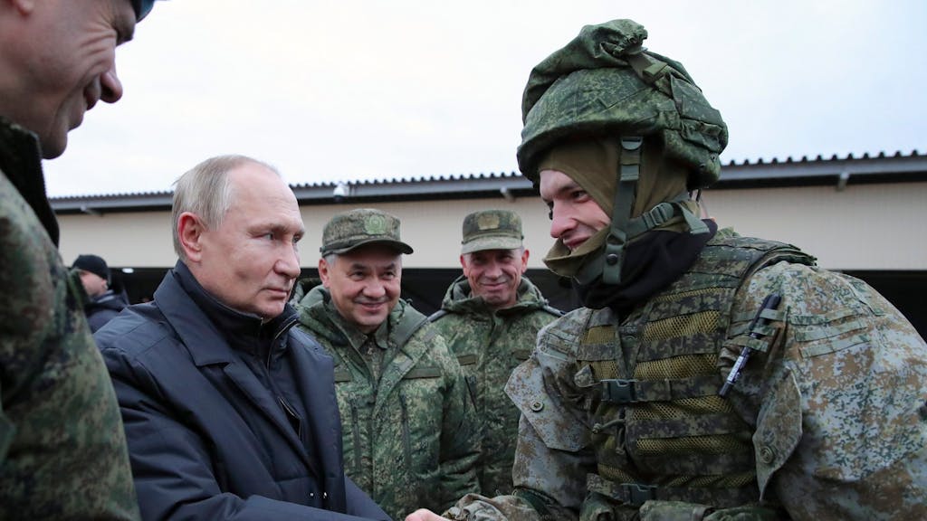 Der russische Präsident Wladimir Putin schüttelt einem Soldaten Mitte Oktober 2022 die Hand, und der russische Verteidigungsminister Sergej Schoigu steht lächelnd neben ihm.
