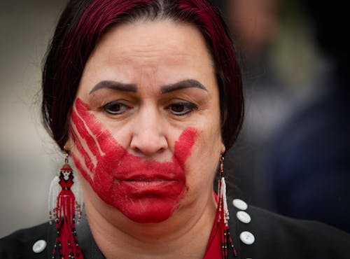05.05.2024, Kanada, New Westminister: Eine indigene Frau trägt im Gesicht einen roten Handabdruck anlässlich des Red Dress Day zum Gedenken an das Leben vermisster und ermordeter indigener Frauen und Mädchen. Der Red Dress Day am 5. Mai findet seit 2010 statt.