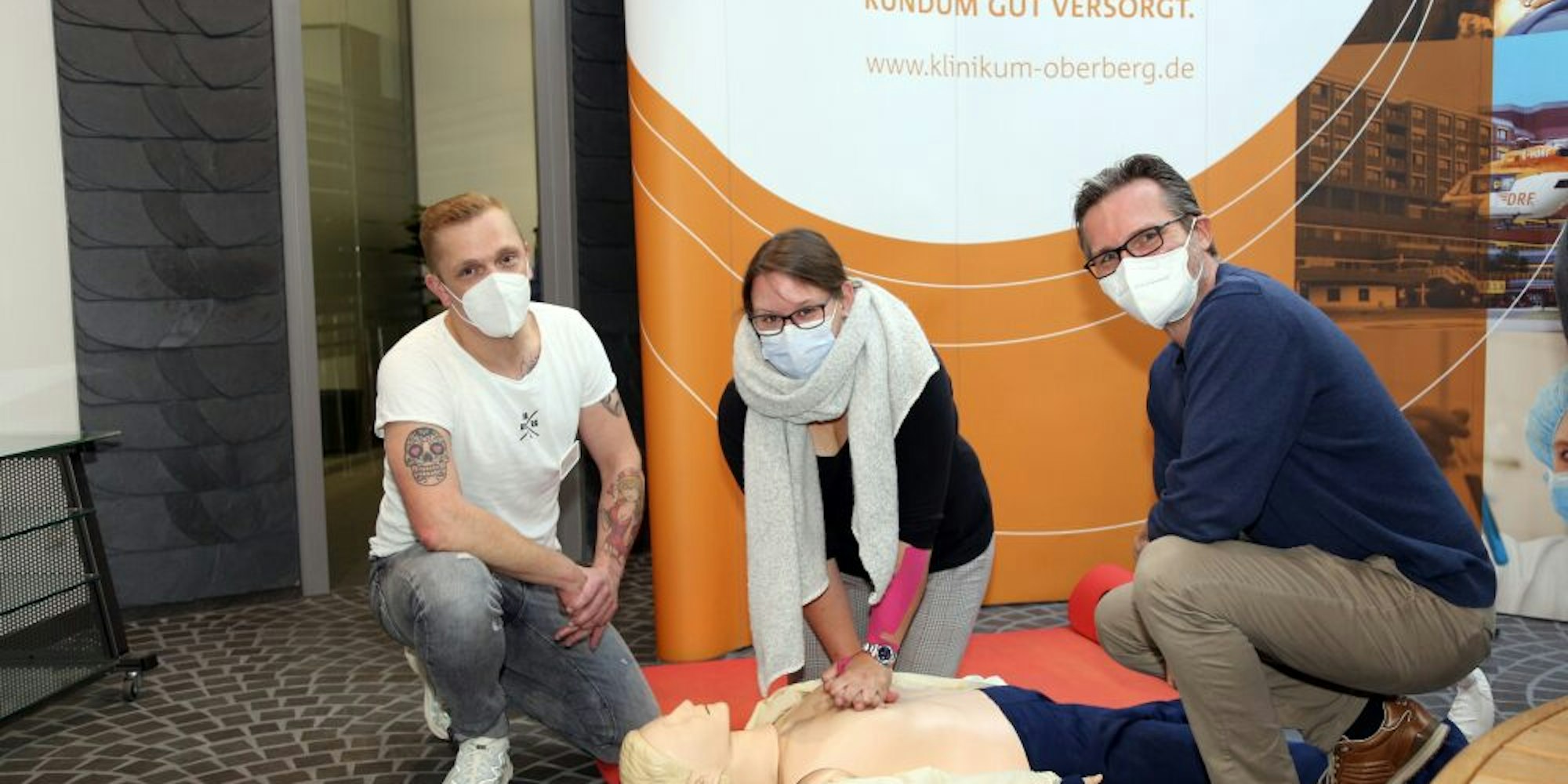 Pfleger Martin Robbins (l.) und Dr. Jörg Niehüser-Saran zeigen Vanessa Tröder, wie die Herzdruckmassage funktioniert.