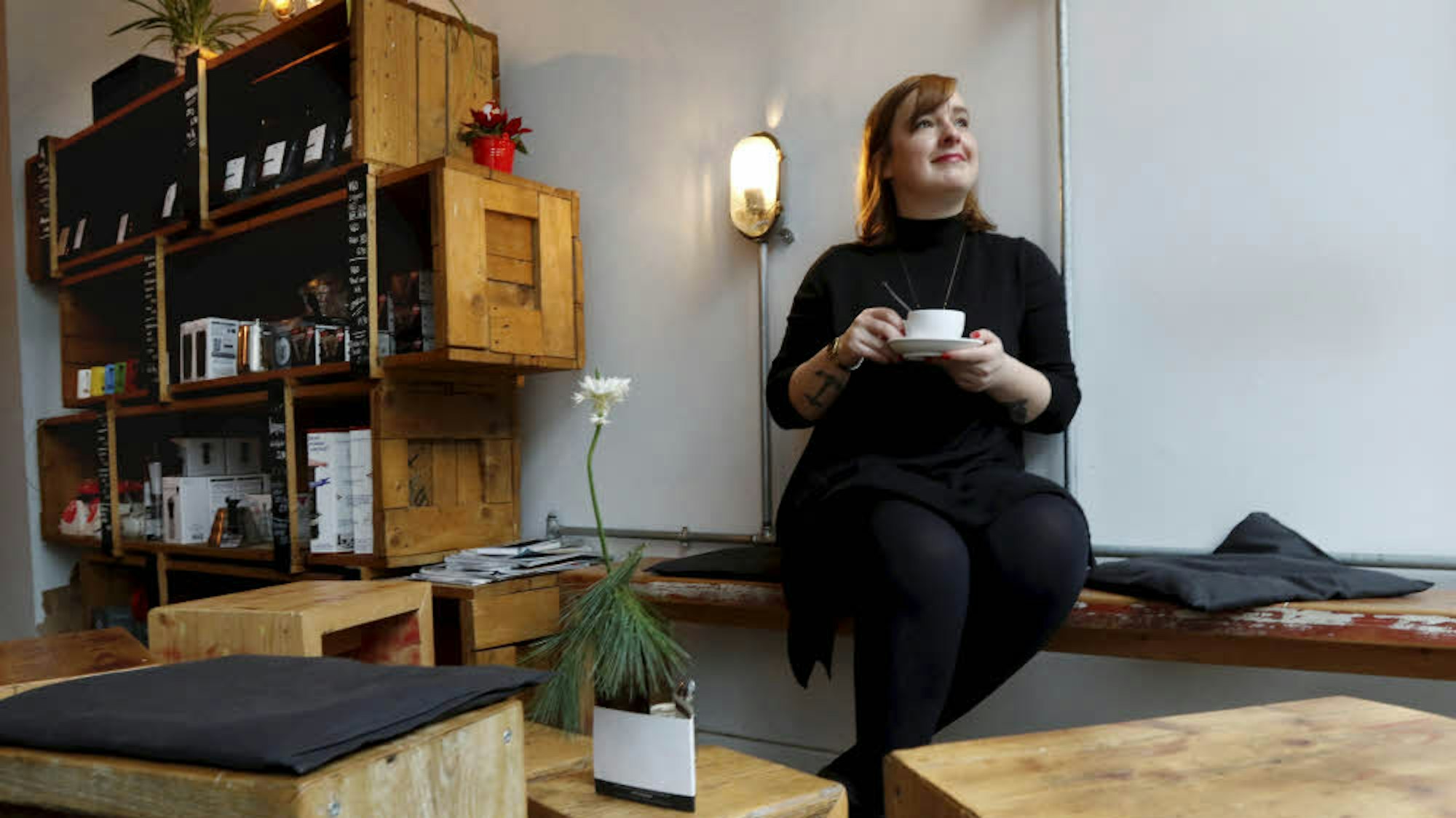 Frau mit Kaffeetasse in der Hand sitzt auf einer Holzbank