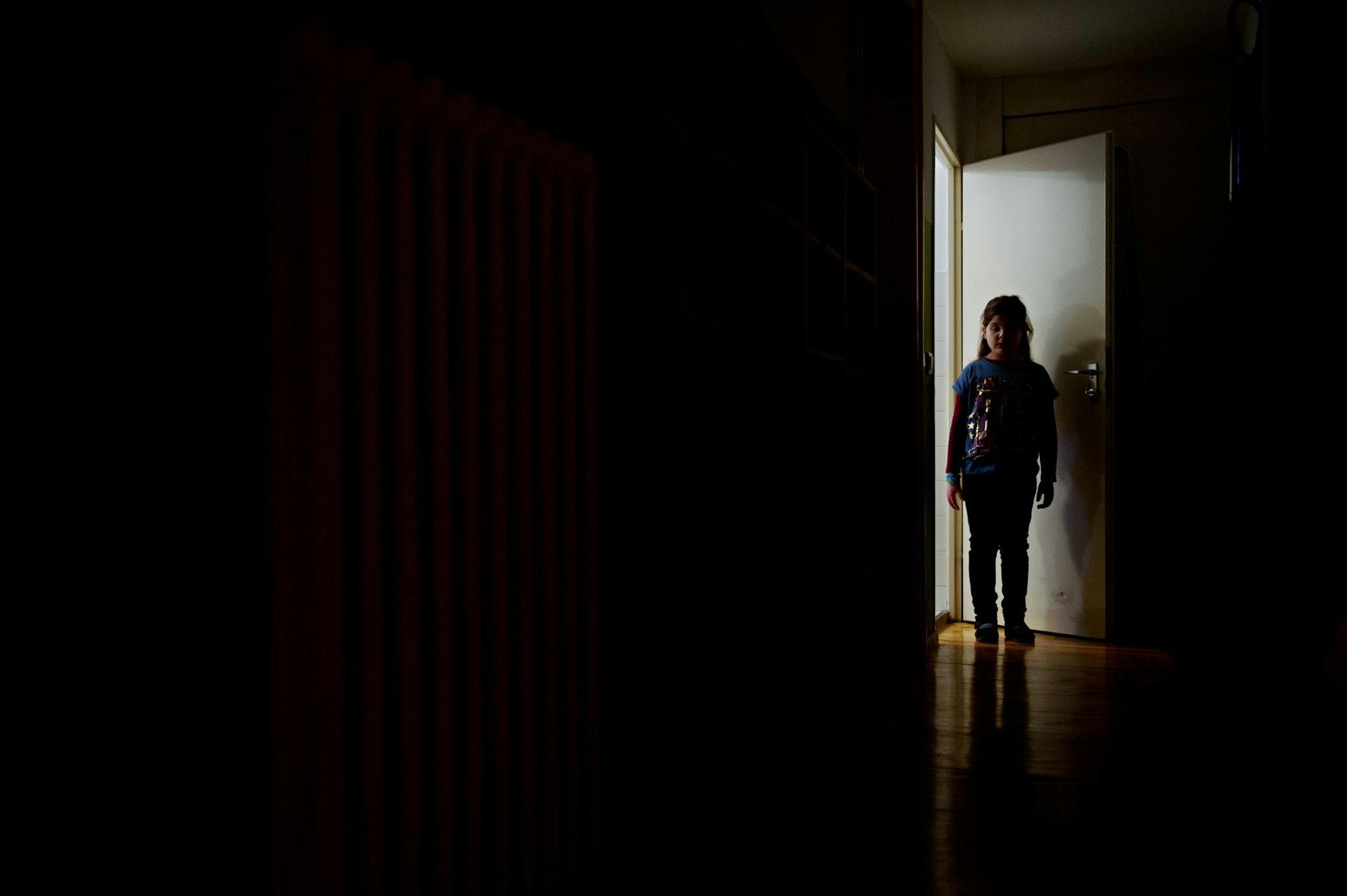 Ein kleines Mädchen steht in der Tür, die in einen dunklen Raum führt.