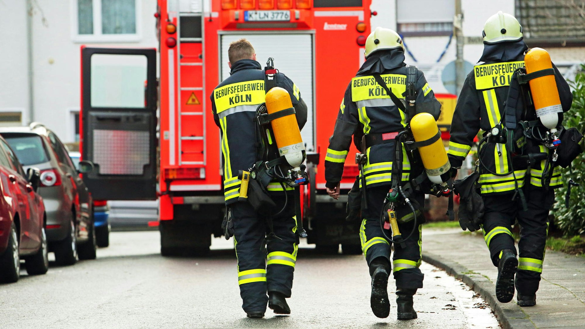 Drei Kölner Feuerwehrleute laufen auf ein Löschfahrzeug zu.