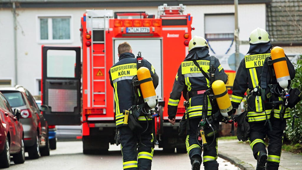Drei Kölner Feuerwehrleute laufen auf ein Löschfahrzeug zu.&nbsp;
