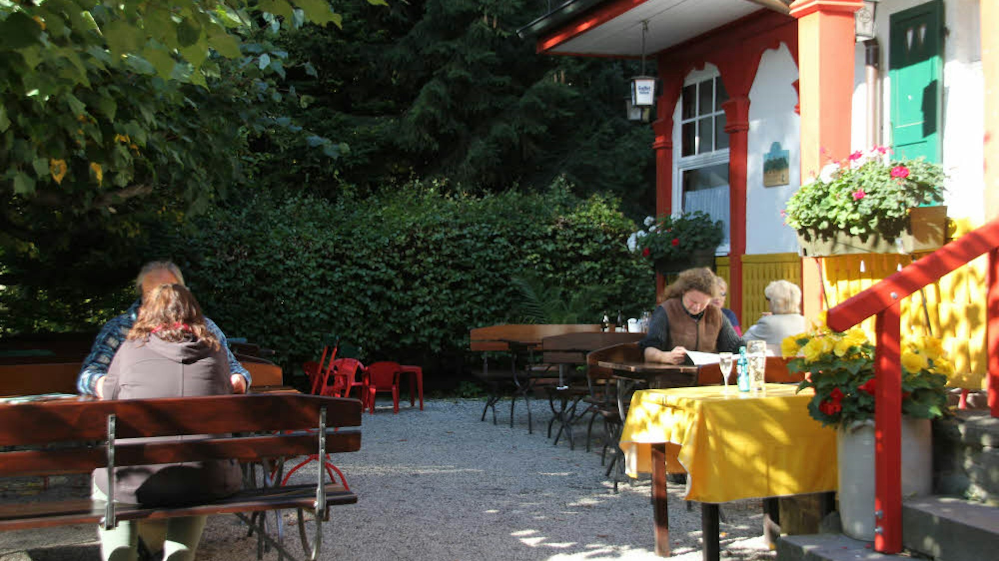 Menschen sitzen an Tischen in der Sonne vor der Gaststätte im Wald