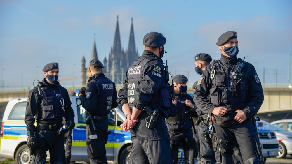 Mehrere Polizisten stehen vor mehreren Streifenwagen, im Hintergrund der Kölner Dom.