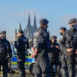 Mehrere Polizisten stehen vor mehreren Streifenwagen, im Hintergrund der Kölner Dom.