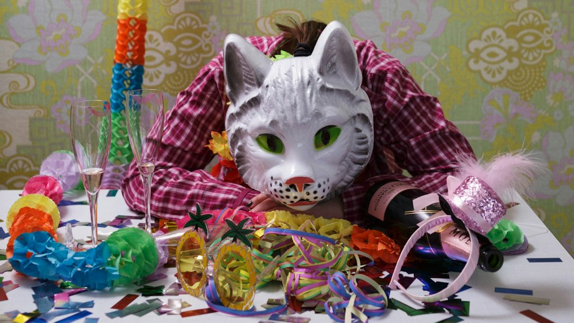 Kostümierter mit Katzenmaske liegt auf einem Tisch mit Luftschlangen.