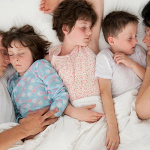 Eltern schlafen mit drei Kindern in einem Bett.