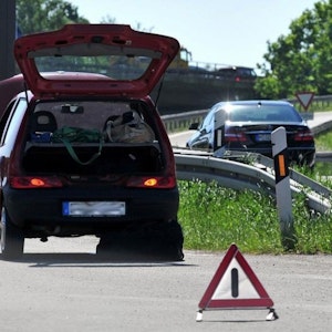 Ein Fahrzeug steht mit geöffnetem Kofferraum am Rand einer Autobahn, davor ein Warndreieck.