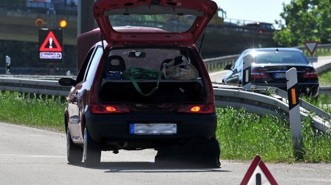 Ein Fahrzeug steht mit geöffnetem Kofferraum am Rand einer Autobahn, davor ein Warndreieck.