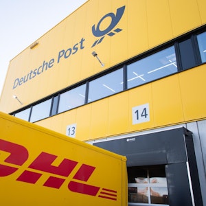 Logos von Deutscher Post und DHL sind auf einem Gebäude und einem Transporter zu sehen.