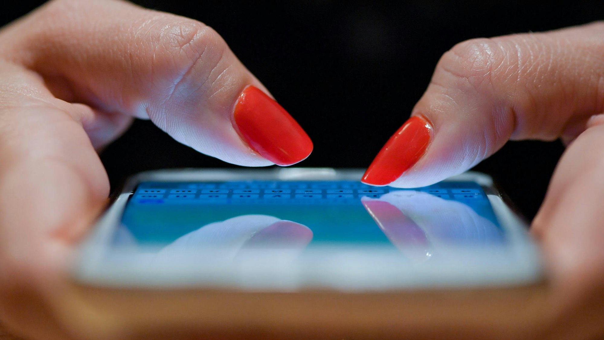 Finger mit rotem Nagellalck tippen auf einem Handybildschirm.