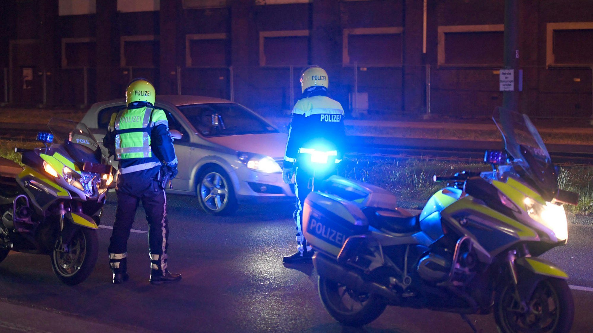 Zwei Polizisten stehen neben ihren Motorrädern und halten ein Auto an.