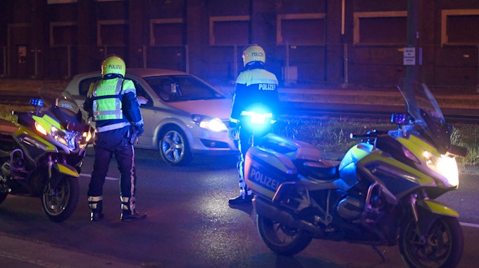 Zwei Polizisten stehen neben ihren Motorrädern und halten ein Auto an.&nbsp;