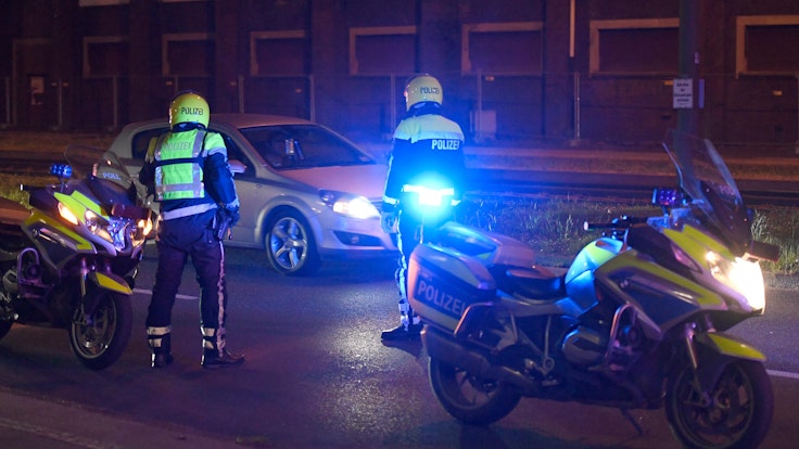 Zwei Polizisten stehen neben ihren Motorrädern und halten ein Auto an.