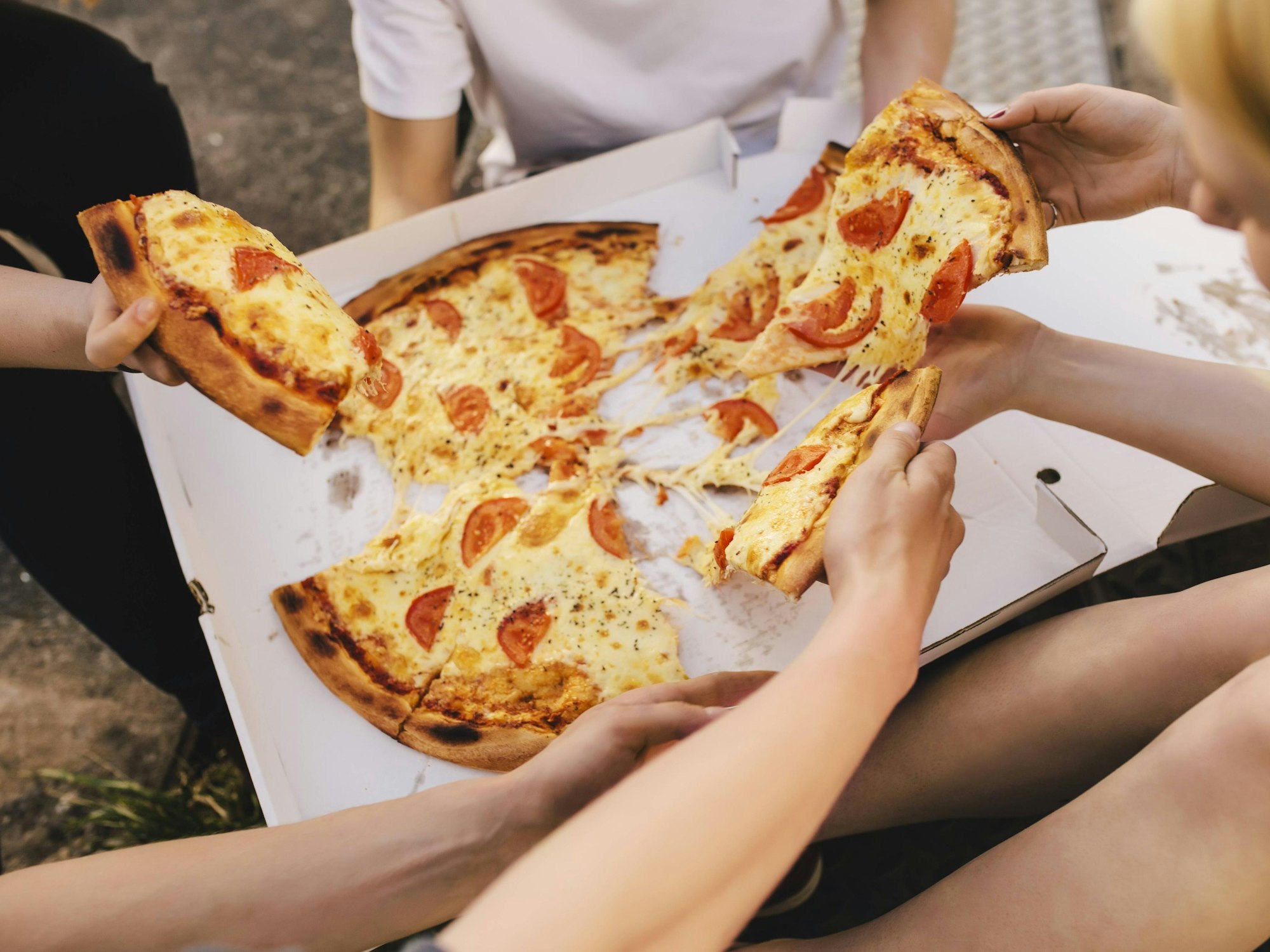 Menschen sitzen auf einer Wiese und teilen eine Pizza.