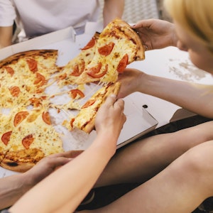 Menschen sitzen auf einer Wiese und teilen eine Pizza.