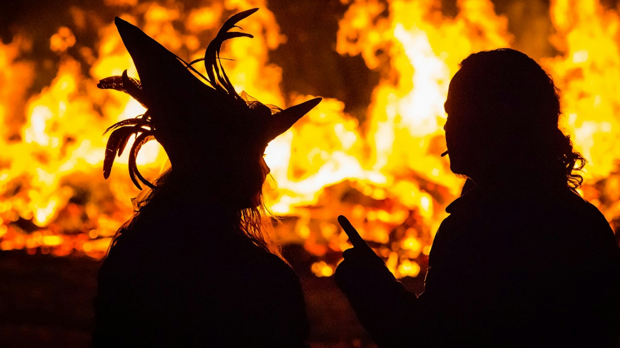 Frau mit Hexenhut und Mann sitzen vor einem Feuer