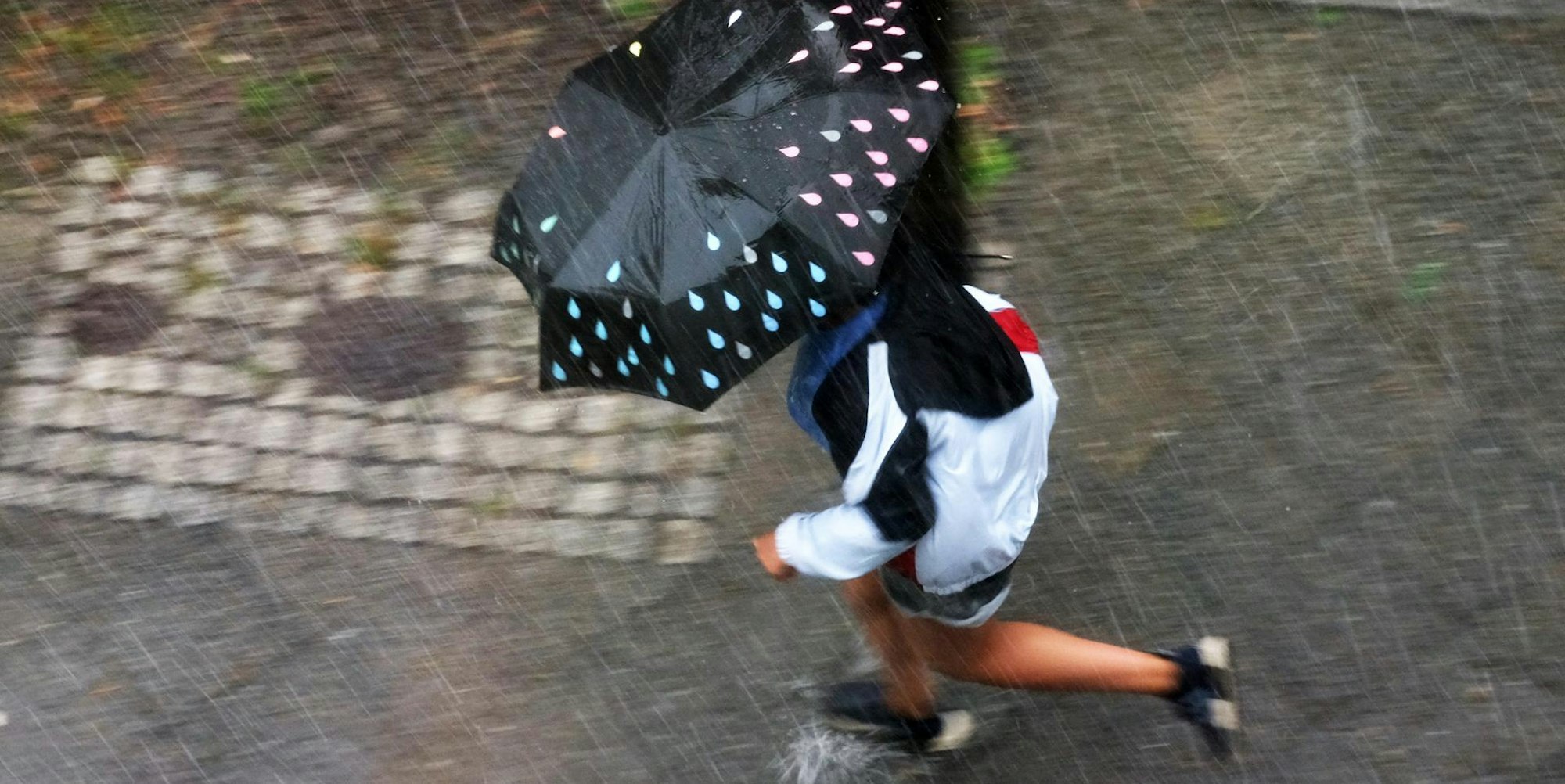 Frau rennt bei einem Sommergewitter mit Schirm herum