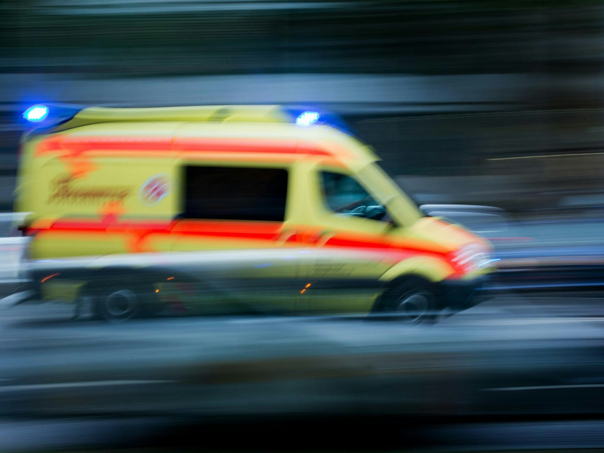 Ein Krankenwagen fährt mit eingeschaltetem Blaulicht eine Straße entlang.
