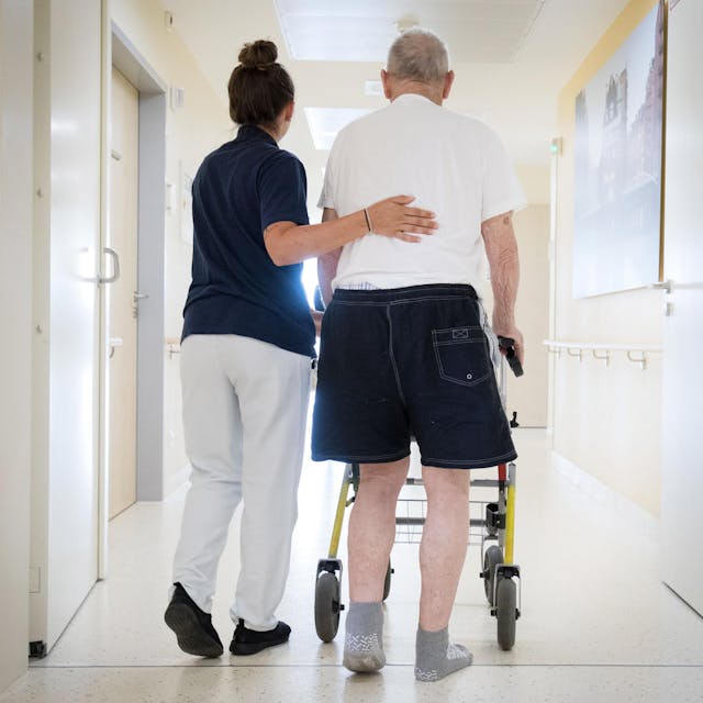 Eine Krankenschwester begleitet einen älteren Mann mit Rollator. (Symbolbild)
