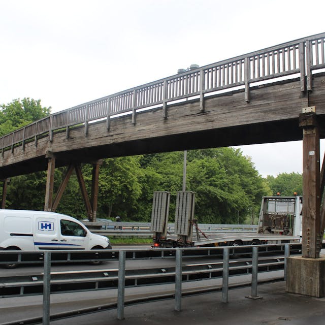 Eine Holzbrücke führt über eine mehrspurige Straße.