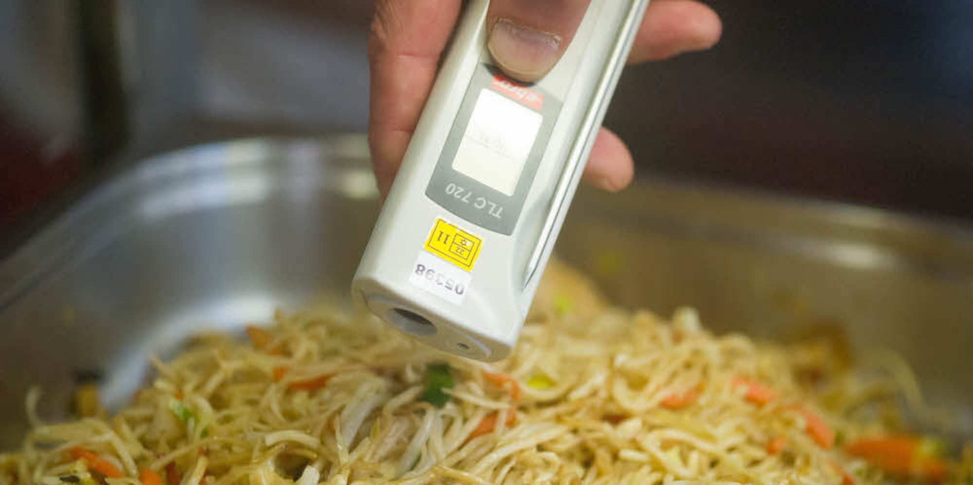 Ein Lebensmittelkontrolleur überprüft die Temperatur eines Nudelgerichts. NRW erhebt seit Mai Gebühren für solche Kontrollen.