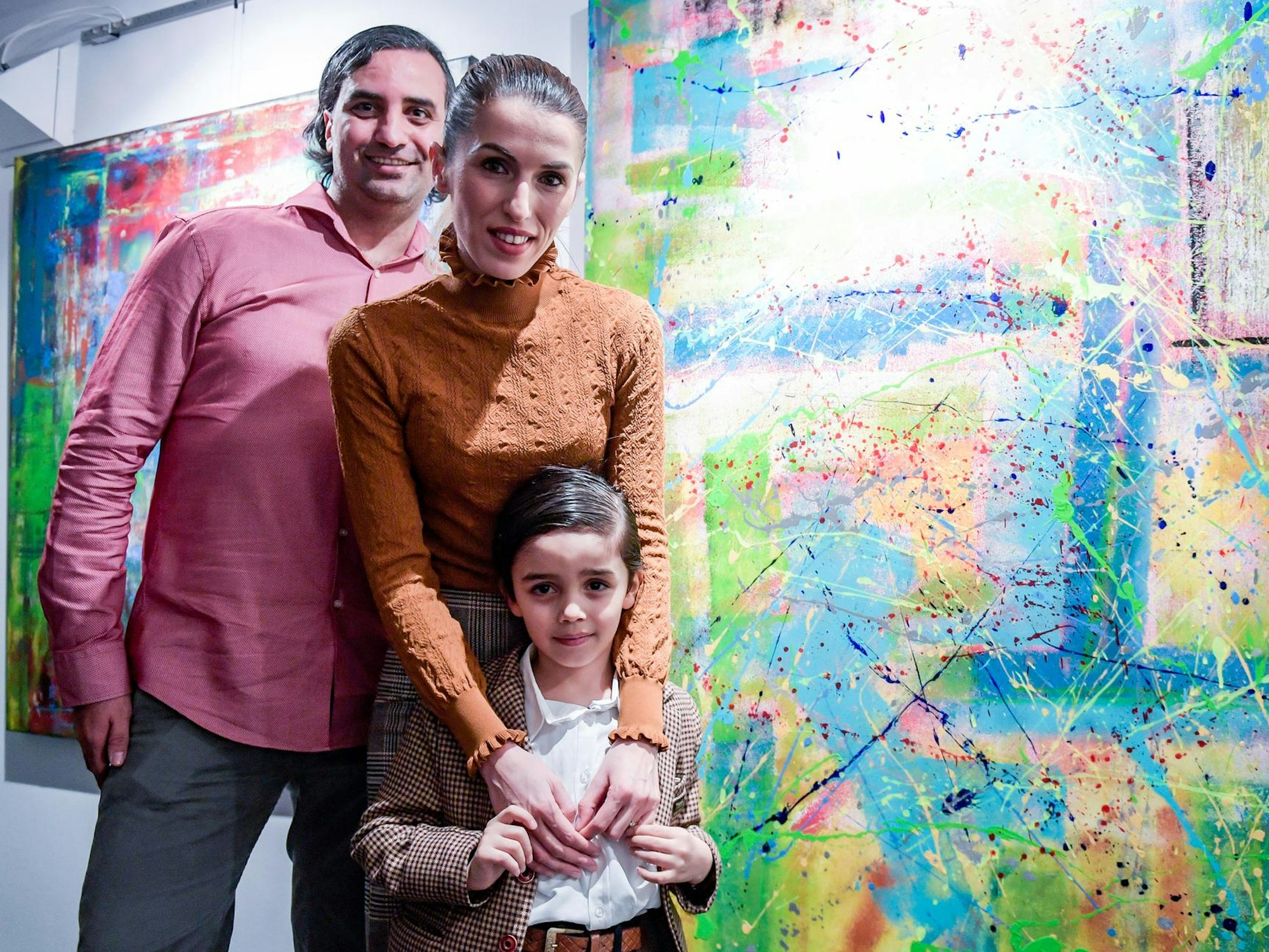 Mikail Akar steht mit seinen Eltern neben einem Gemälde.
